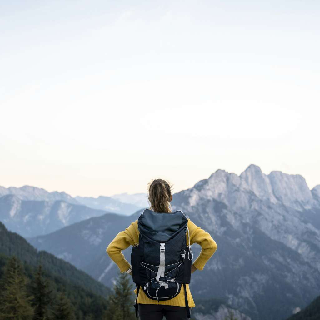 View from behind of a female hiker with backpack standing on top of a mountain